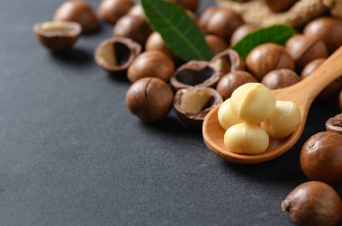 Siyah taş zemin üzerine tahta kaşık macadamia fındık. superfood ve sağlıklı gıda kavramı