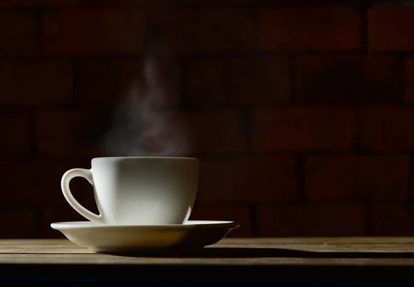 Hot coffee cup with smoke on wood table and old brick background