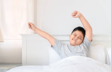 Obses şişman çocuk pijama yatağa oturmuş ve germe. Günaydın dünya