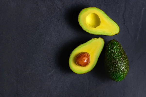 Aguacate fresco. Fruta de aguacate en rodajas sobre piedra negra — Foto de Stock