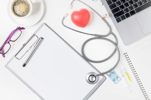 Top view of doctor desk table with stethoscope, coffee  and blank paper on clipboard with pen. Top view with copy space, flat lay.