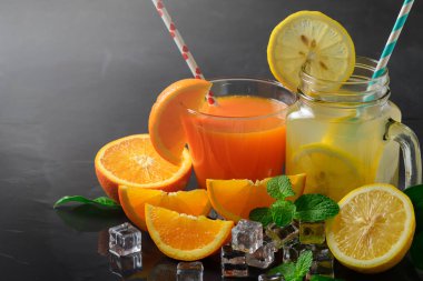 Portakal suyu ve limon suyu ile taze dilim portakal ve dilim limon siyah taş zemin üzerine yaz içecekler kavramı