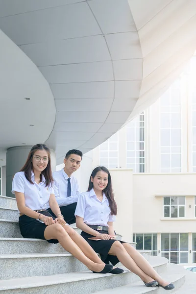 Щасливі азіатські студенти в уніформі сидячи в університеті — стокове фото