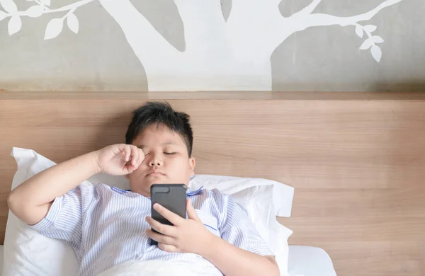 Boy rubbing eyes after play smartphone