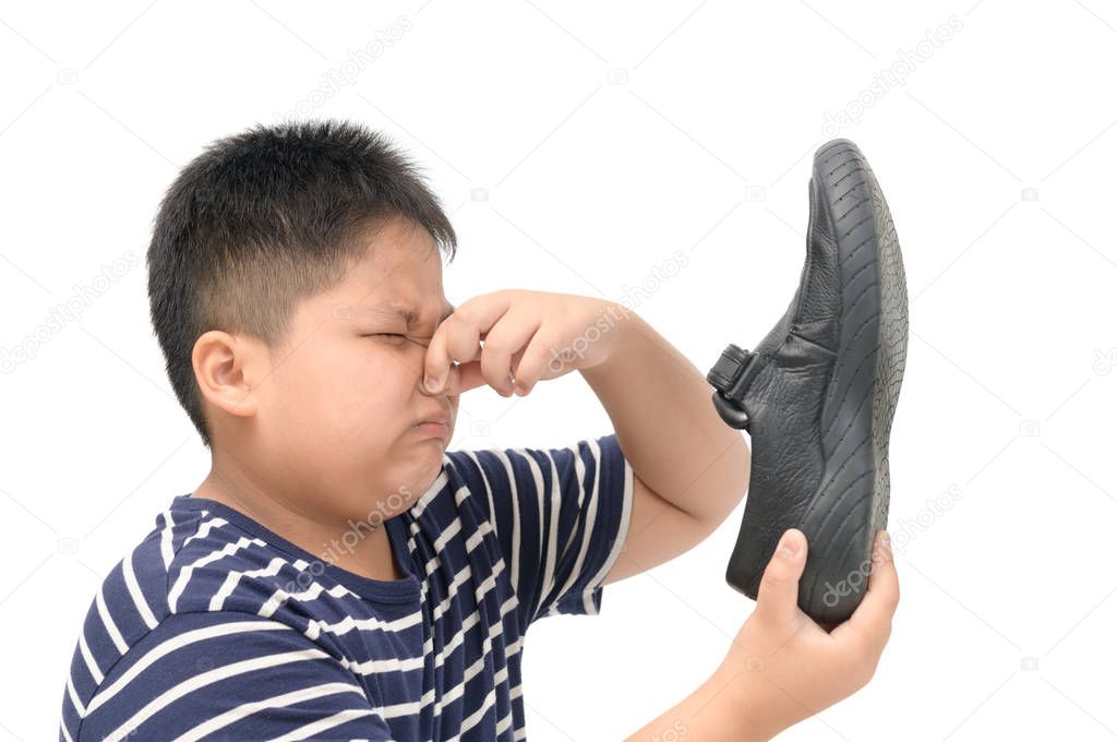 Disgusted boy holding a pair of smelly leather shoes 