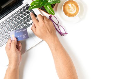 Beyaz masadan online alışveriş için kredi kartı kullanan bir adam beyaz arka planda izole edilmiş kahve, üst görünüm ve metin için kopyalama alanı olan bir kahve tablosu kullanıyor. Çevrimiçi alışveriş ve yeni normal kavram.