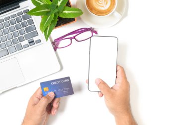 Akıllı telefon ve kredi kartını kullanarak beyaz masadan alışveriş yapıyor. Beyaz arka planda, en üstteki manzarada ve yazılı metinde, sütlü kahve izole edilmiş. Çevrimiçi alışveriş ve yeni normal kavram.
