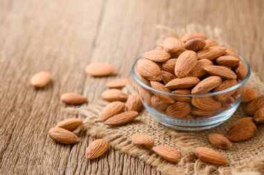 Badem fındıkları cam kasede soyularak ahşap masada güneş ışığıyla birlikte. Badem çok popüler bir fındık ve yüksek proteindir. sağlıklı yiyecekler.