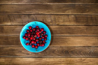 Ahşap bir masada, üzerinde kiraz olan mavi bir tabak.