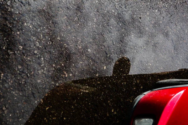 Fragment of a red car and its reflection on the asphalt