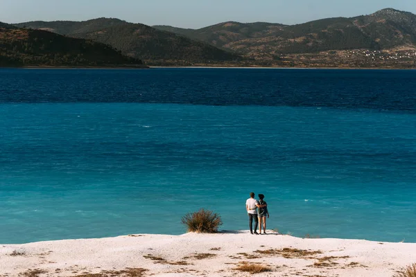 一对恋爱中的夫妇看着蓝色的泻湖 一对恋爱中的情侣在海滩上 蜜月爱好者 岛上的男人和女人 一对恋爱中的情侣在度假 男人和女孩拥抱 海上旅游 情侣旅行 — 图库照片