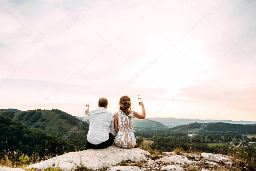 Couple in love drinking champagne. Man and woman celebrating their engagement. Newlyweds drink champagne. Couple meets sunset. Boy and girl greet the dawn. Guy and girl with their backs to the cam