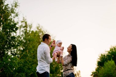 Mutlu Aile parkı akşam ışık. Bir güneş ışıkları. Anne, baba ve bebek mutlu gün batımında yürümek. Mutlu bir aile kavramı. Ebeveynler bebeğin ellerini tutun