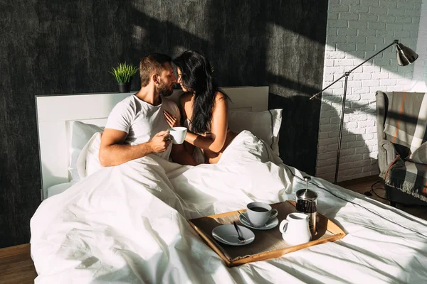 ベッドの美しいカップル。ベッドでは恋人。幸せな夫婦のベッドで朝食を持っていること。家族関係。若いカップルがお茶を飲みます。男性と女性が彼らの寝室で朝食をとり — ストック写真