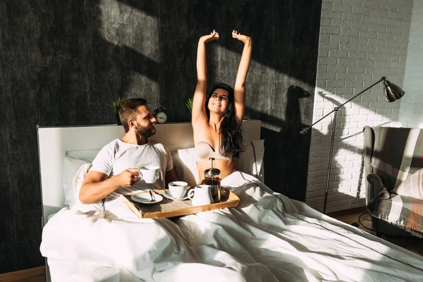 Beautiful couple in bed. Lovers in bed. Happy loving couple having breakfast in bed. Family relationships. Young couple drinking tea. Man and woman having Breakfast in their bedroom — Stock Photo, Image