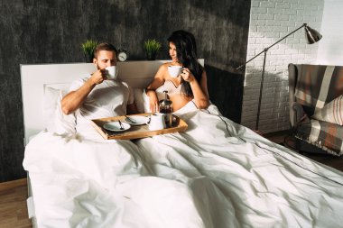 Güzel çift yatakta. Aşıklar yatakta. Mutlu sevgi dolu çift yatakta kahvaltı. Aile ilişkileri. Genç çift çay içme. Erkek ve kadın kendi yatak odasında kahvaltı