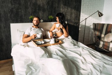 Güzel çift yatakta. Aşıklar yatakta. Mutlu sevgi dolu çift yatakta kahvaltı. Aile ilişkileri. Genç çift çay içme. Erkek ve kadın kendi yatak odasında kahvaltı