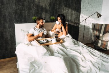 Güzel çift yatakta. Aşıklar yatakta. Mutlu sevgi dolu çift yatakta kahvaltı. Aile ilişkileri. Genç çift çay içme. Erkek ve kadın kendi yatak odasında kahvaltı