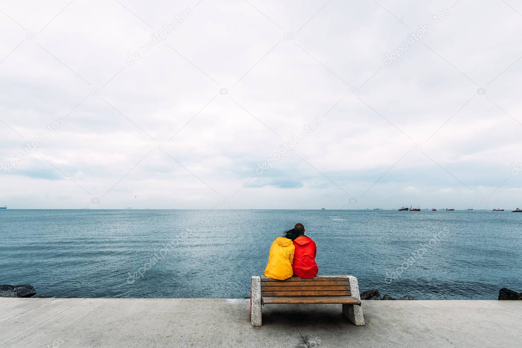 Young couple sitting on a bench by the sea. Man and woman traveling. People sit on a bench and look at the sea. Tourists by the sea. Friends on the bench. A lonely pair. Walking along the promenade