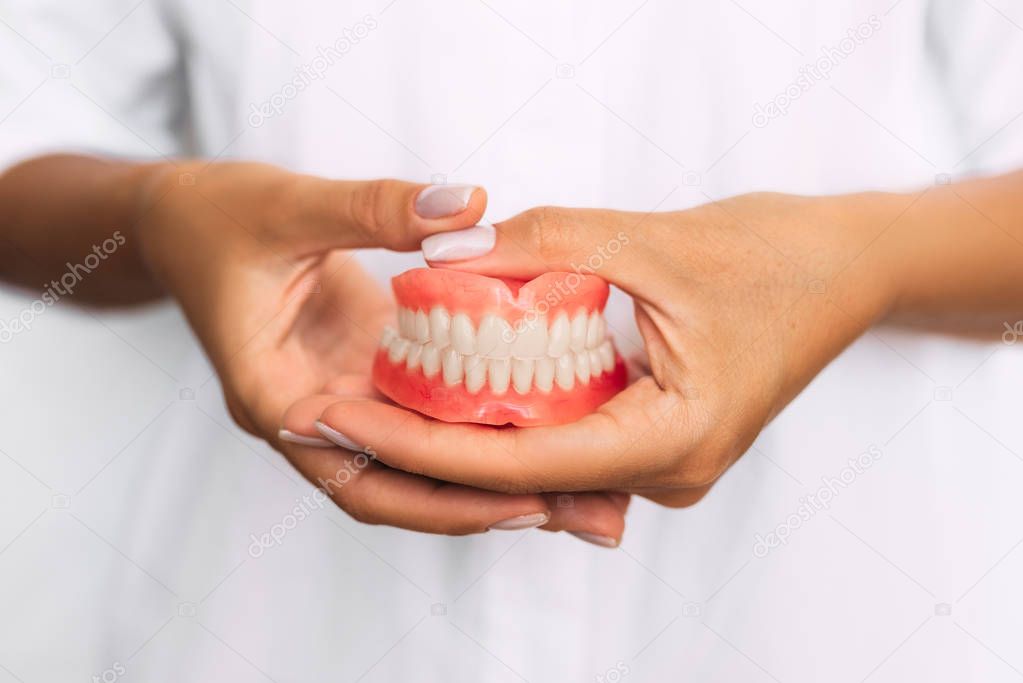 The dentist is holding dentures in his hands. Dental prosthesis in the hands of the doctor close-up. Front view of complete denture. Dentistry conceptual photo. Prosthetic dentistry. False teeth