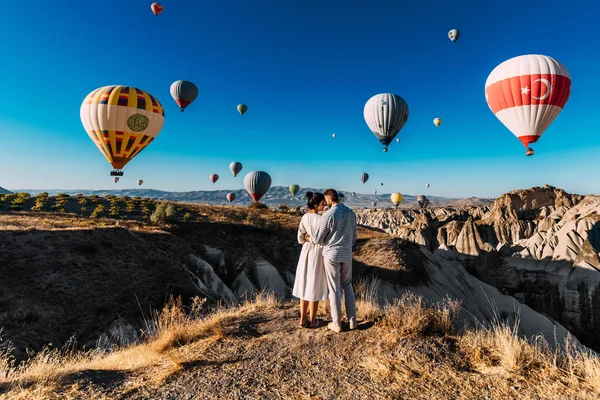 Una pareja viaja por el mundo. Viaje de luna de miel. Pareja casada de vacaciones. Turistas en Capadocia. Hombres y mujeres descansando en Turquía. Globos voladores al amanecer. Una gira mundial. Hombre y mujer entre globos —  Fotos de Stock