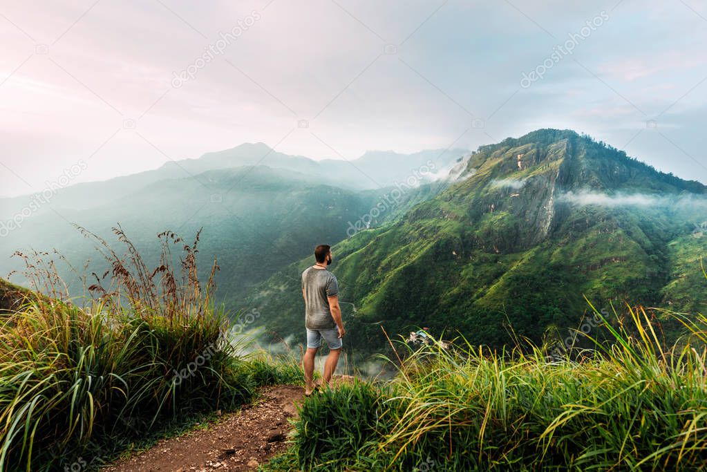 A man stands with his back in the mountains. A man travels in Asia. Travel to Sri Lanka. Traveler in the mountains. A man enjoys a beautiful view of the mountains. Man at sunrise in the mountains