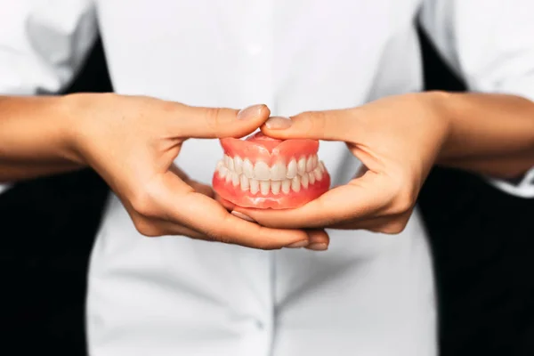 The dentist is holding dentures in his hands. Dental prosthesis in the hands of the doctor close-up. Front view of complete denture. Dentistry conceptual photo. Prosthetic dentistry. False teeth