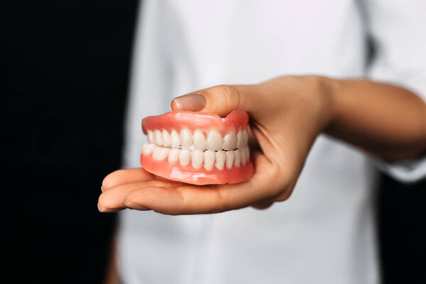 The dentist is holding dentures in his hands. Dental prosthesis in the hands of the doctor close-up. Front view of complete denture. Dentistry conceptual photo. Prosthetic dentistry. False teeth