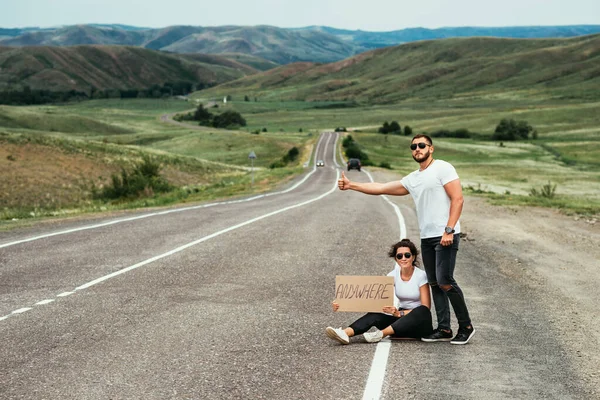 A young couple hitchhiking around the country. A couple in love stops the car at the road. Travel by car. A man and a woman with a sign by the road. Copy space. The couple goes traveling