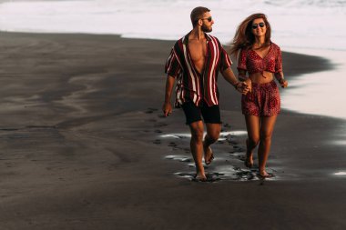 Aşık bir çift gün batımında plaj boyunca koşar. Bir erkek ve bir kadın sahilde eğleniyor. Mutlu çift sahilde eğleniyor. Kumsalda eğlenen bir çift. Uzayı kopyala Bali 'de Tatil
