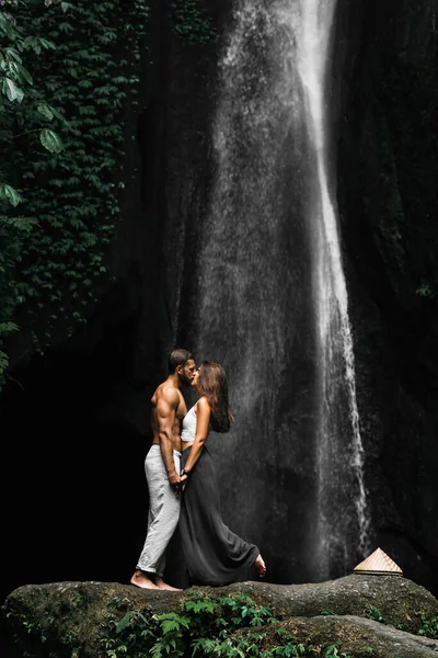 インドネシアの滝で美しいカップル 愛のカップルはバリの島の周りを旅します 滝で男と女がキスをする アジアへの旅行 新婚旅行だ 滝の観光客 — ストック写真