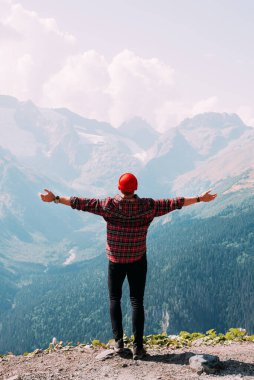 Kolları açık bir şekilde dağların arka planında dikilen bir adamın arkası. Dağdaki adam ellerini kaldırdı. Dağların arka planında bir adam. Dağlara git.