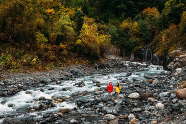 Genç bir çift İskandinav yürüyüşü yapıyor. Doğada aktif dinlenme. Sonbaharda bir dağ nehri boyunca yürüyen iki turist. Yürüyüş 'te aktif bir çift var. Genç bir çift iz sürmekle meşgul. Boşluğu kopyala