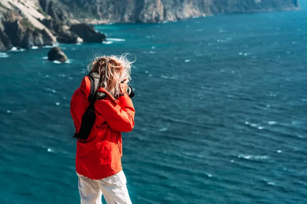 赤いジャケットの旅行者の写真家は カメラ リアビューで海の写真を撮る 背景の海に写真カメラで海の風景を作る観光客の旅行者写真家 スペースのコピー — ストック写真