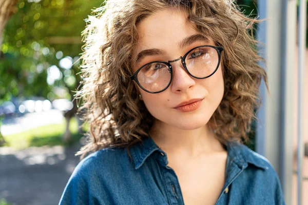 Ao ar livre perto retrato de jovem bonita e elegante menina sorridente encaracolado usando óculos de sol, posando na rua. Luz do dia ensolarada. Conceito de moda de verão. Copiar, espaço vazio para texto — Fotografia de Stock