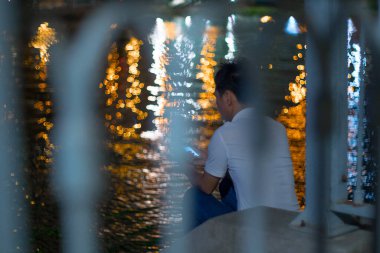 Arka planda gölün kenarında akıllı telefonu olan bir adam oturuyor.