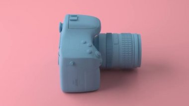 Serin profesyonel mavi kamera kendi ekseni etrafında döner. Arka plan moda pembe ve pastel renkte boyanmış. En az tarzı resimde. 3D render.