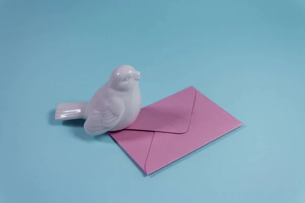 White bird with invitation messages letter in bright pink envelope on pastel blue background. Communication greeting concept