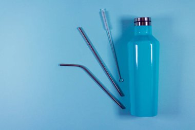Çevre dostu sıfır atık yaşam tarzı, yeniden kullanılabilir termos su şişesi ve pastel mavi arka planda paslanmaz içme pipetleri, yeşil ve plastiksiz konsept