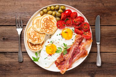 İki omlet, krep, domates salatası, domuz pastırması ve yeşil zeytinli Amerikan kahvaltısı. en üstteki görünüm
