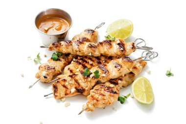 Beyaz arka planda fıstık ezmesi soslu ızgara tavuk şişleri.