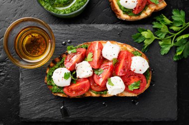 Kirazlı domates, mozzarella peyniri ve siyah arkaplanda pesto sosu. Geleneksel İtalyan aperatifi veya aperatifi, antipasto.Üst görünüm