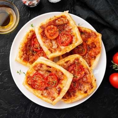 Puf böreği, peynirli mini turtalar ve siyah arka planda domatesler.