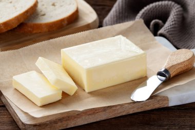 Kesme tahtasının üzerinde dilimlenmiş tereyağı parçaları, ahşap arka plan. Bir parça tereyağı.