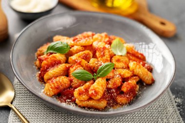 Geleneksel İtalyan patates gnocchi domates sosu, parmesan peyniri ve gri arka planda taze fesleğen yaprakları.