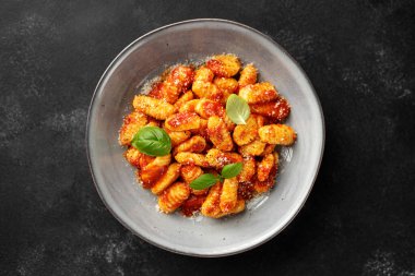 Domates soslu geleneksel İtalyan patates gnocchi 'si, parmesan peyniri ve siyah arka planda taze fesleğen yaprağı, üst manzara.