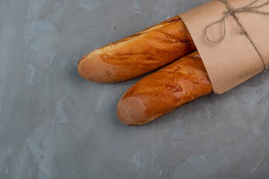 Gri desenli bir arka planda kağıt bir torba içinde taze pişmiş baget..