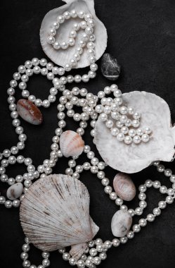 Siyah bir zemin üzerinde doğal incilerden yapılmış mücevherler, deniz kabukları ve deniz taşları. Yukarıdan görünüşü.