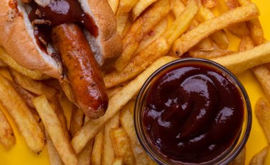 Kızartmaların üzerinde sosisli ve ketçap var. Sarı parlak arka plan. Yemek arkaplanı. Yukarıdan görüntüle.