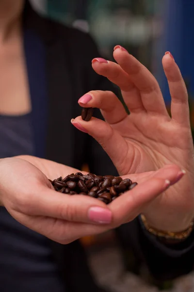 Close-up of girl\'s hands showing roasted coffee bean in her fingers with blurred background behind.